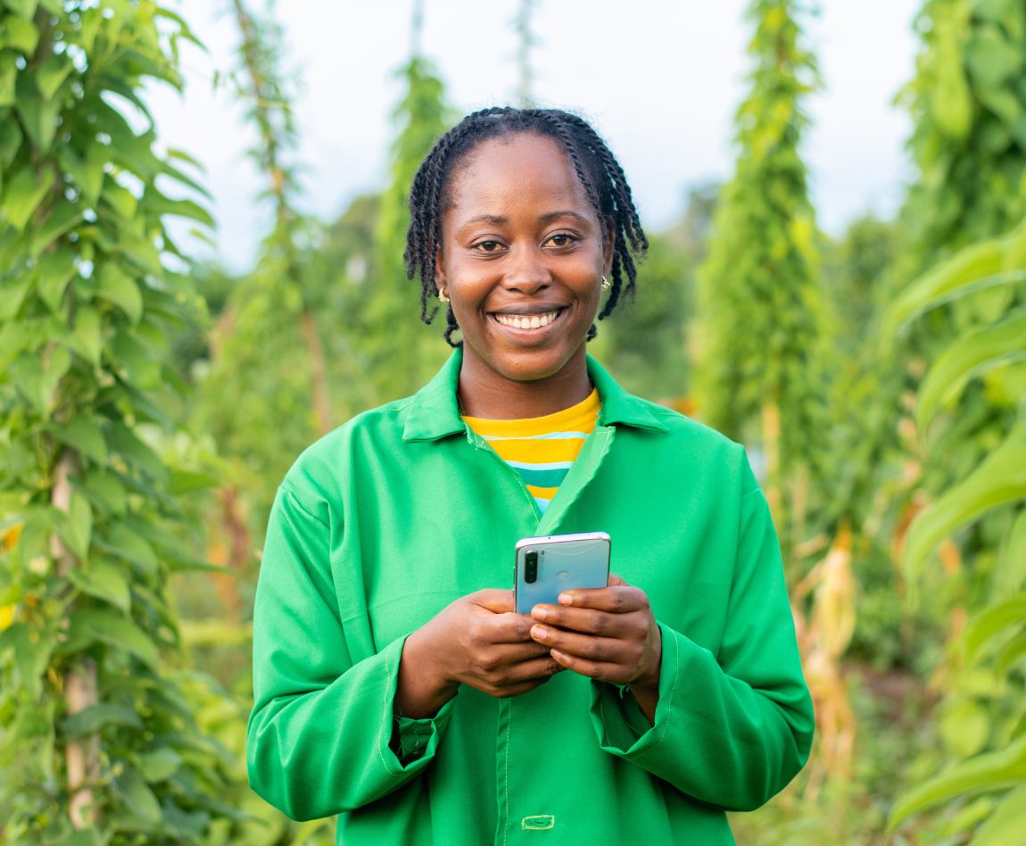 Une femme d'origine africaine tient un smartphone dans ses mains, elle se trouve dans un champ