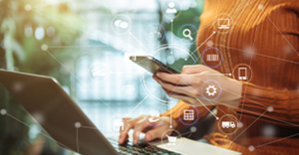 Femme utilisant un ordinateur portable et un smartphone avec des icônes numériques superposées, illustrant la transformation digitale.