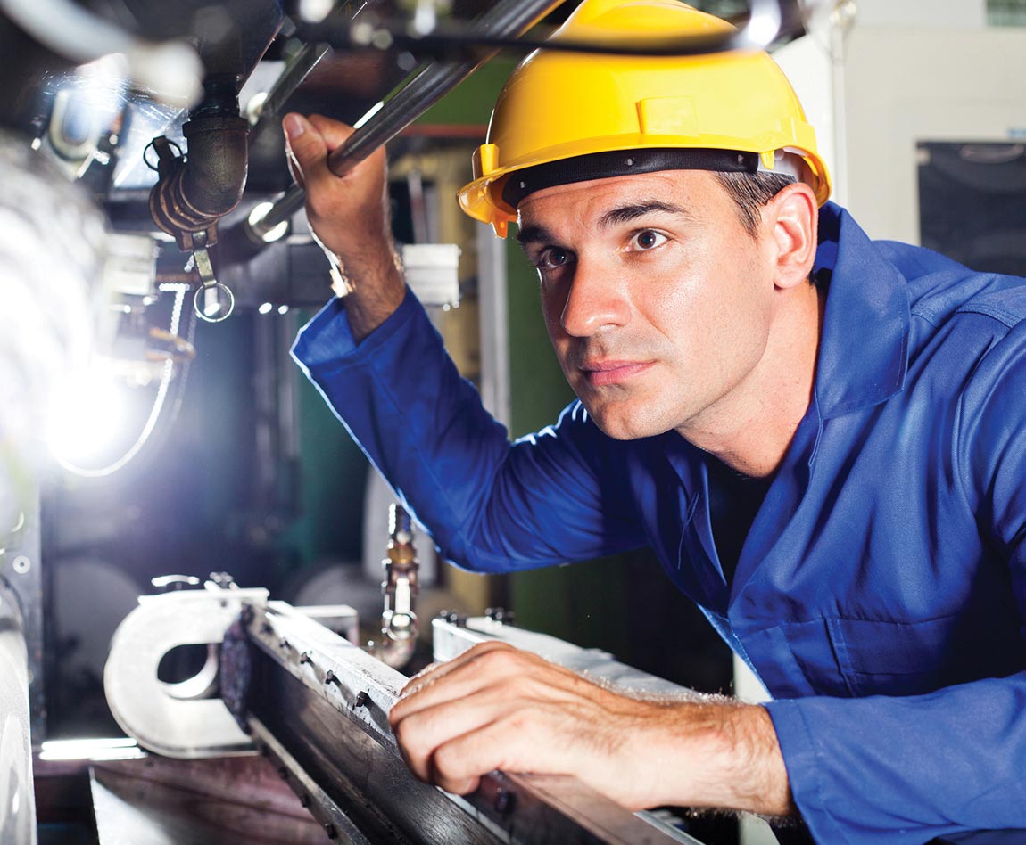 A maintenance worker with a yellow construction helmet examines an industrial machine.
